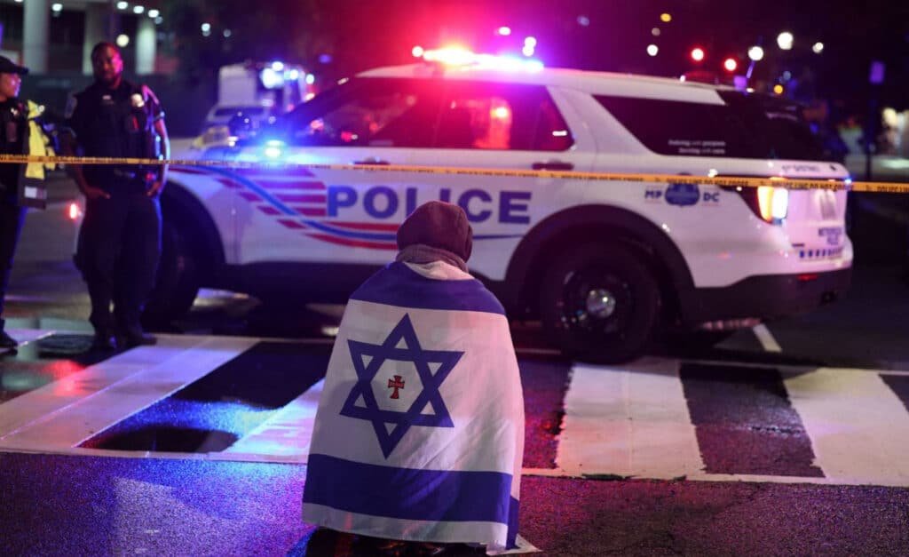 A mourner draped in an Israeli flag 🇮🇱 kneels on a D.C. street, surrounded by police cars with flashing lights 🚨 and crime scene tape. This haunting scene captures the aftermath of the Capital Jewish Museum shooting, where 2 Israeli embassy staff were killed. We stand with the Jewish community. 🙏 #DCJewishMuseumShooting #Antisemitism #StandWithIsrael #Trump2025 #JusticeForVictims