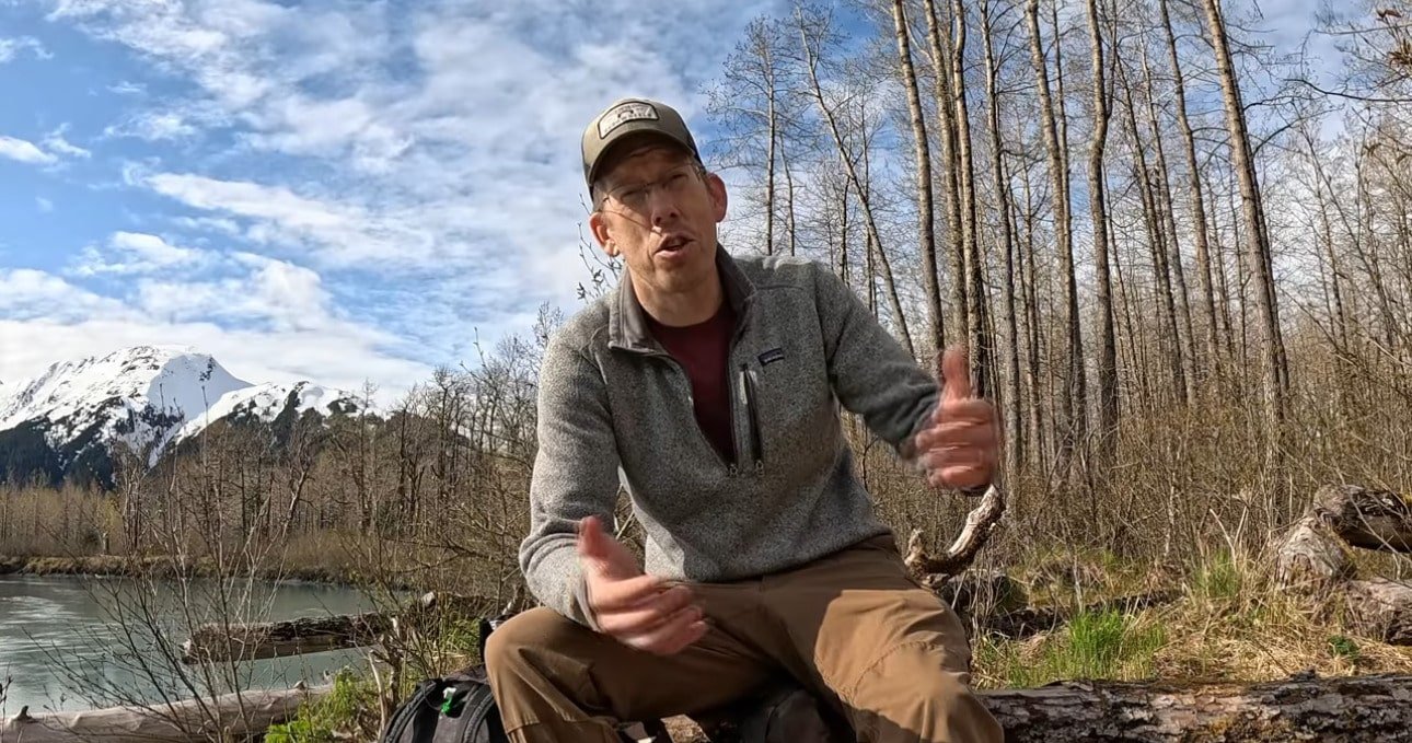 Luke Nichols of Outdoor Boys YouTuber waves goodbye from a stunning Alaskan wilderness, with snow-capped mountains and a river behind him! Dressed in rugged gear, he’s breaking hearts by quitting YouTube to focus on family—a true MAGA move. JV Political salutes this patriot—share to keep his legacy alive! See Ya