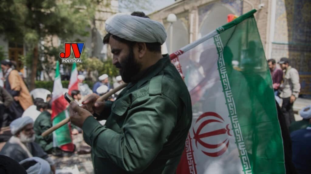 Intense scene of a bearded man in a green uniform proudly waving the Iranian flag amidst a crowd of protesters, with the historic backdrop of a tiled mosque and other flag-bearers in the background. The JVPolitical logo marks this powerful image of national pride and resistance. #IranPride #IranProtests #MAGA #AmericaFirst #JusticeForIran #StrongLeadership #Trump2024 #FreedomFight #IranStrong #PatriotNation
